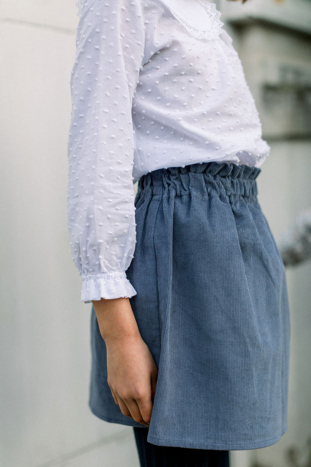A person wearing a blue corduroy skirt with an elastic high waist, paired with a white blouse.