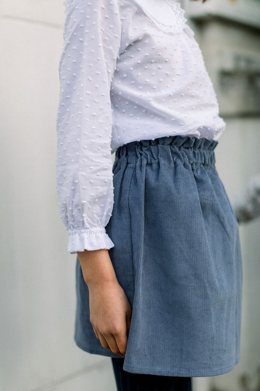 A person wearing a blue corduroy skirt with an elastic high waist, paired with a white blouse.