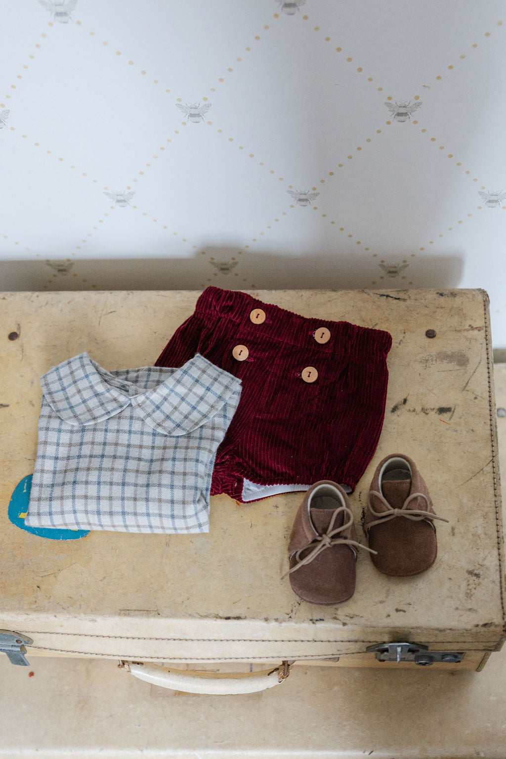 Children's clothing and shoes on an old suitcase with a patterned wall in the background