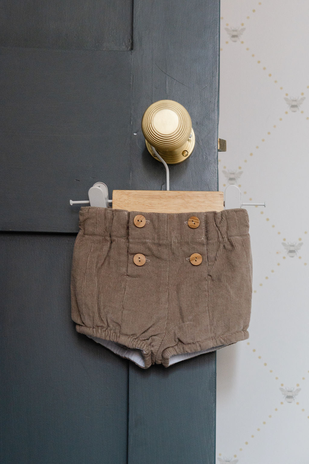 Brown shorts hanging on a door handle against a dark wall.