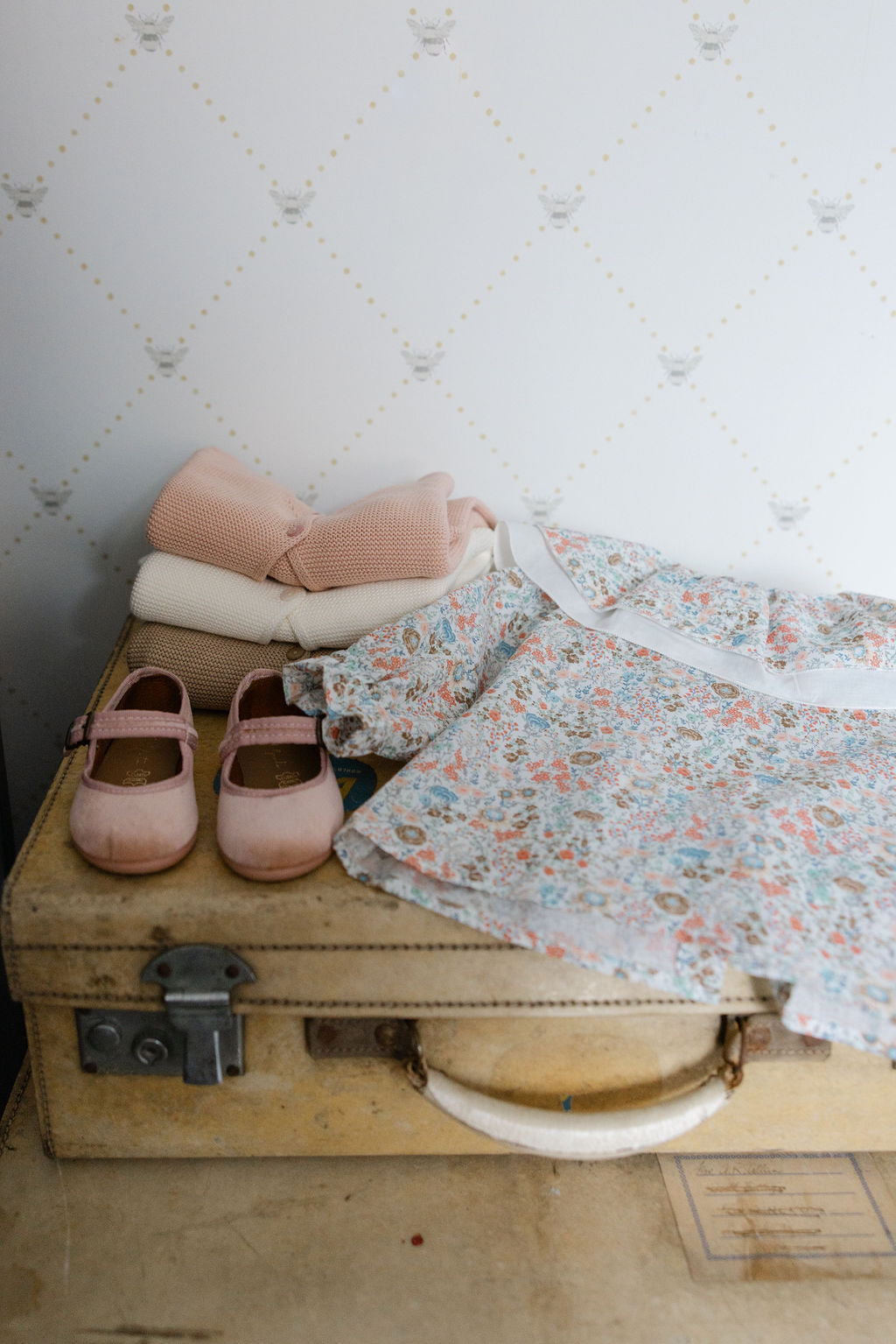 Vintage suitcase with baby shoes, clothes, and a blanket on a textured wall background
