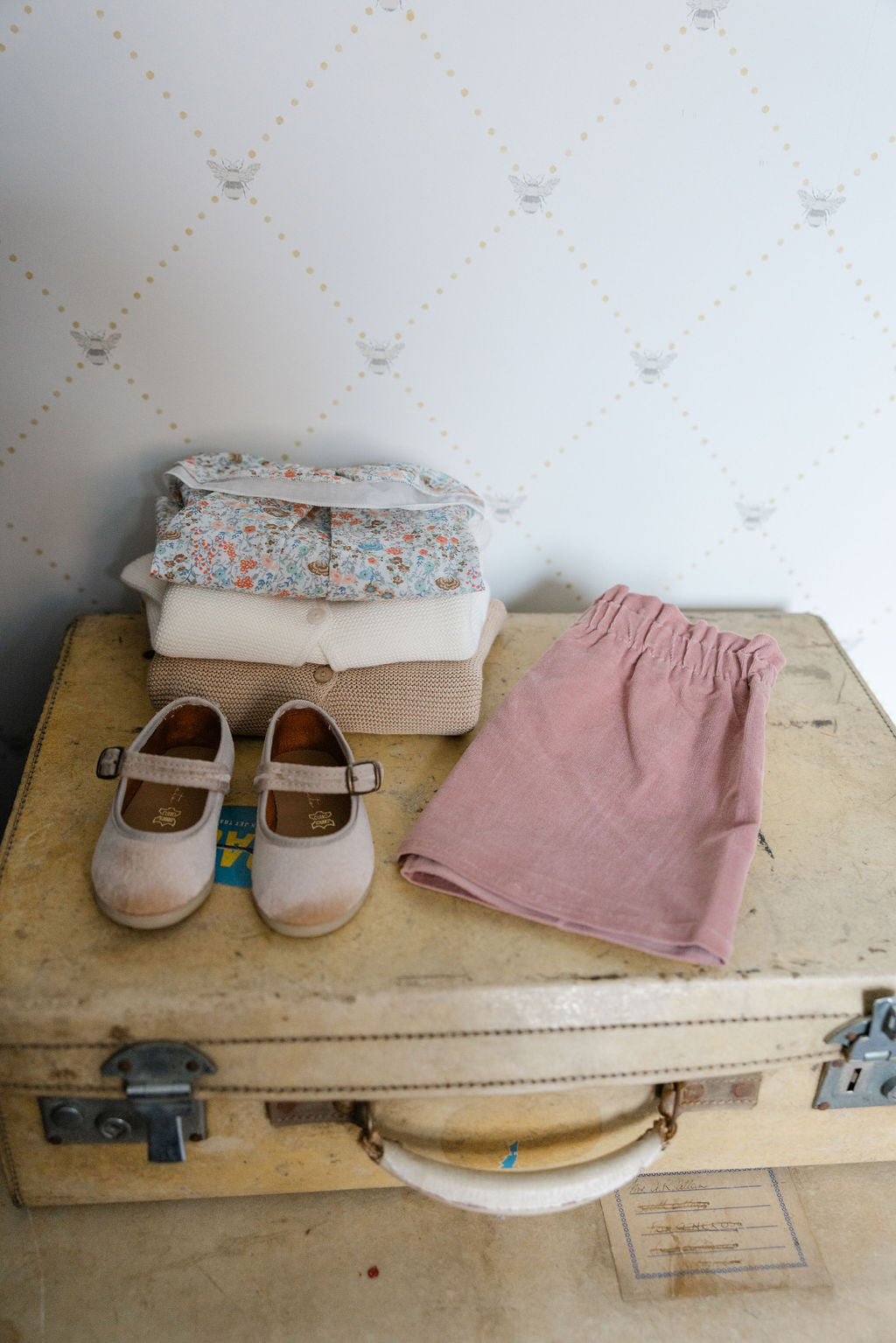 Vintage suitcase with pink pants, white shoes, and folded clothes on a textured wall background
