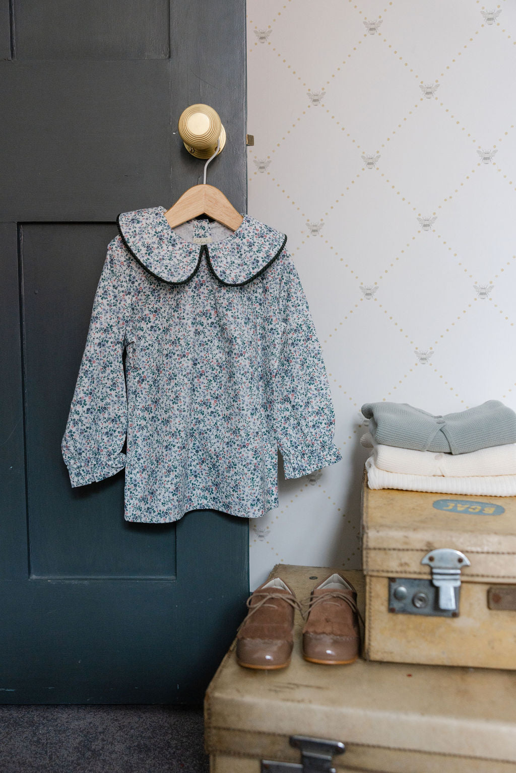 Floral blouse with black collar on a hanger against a textured wall.