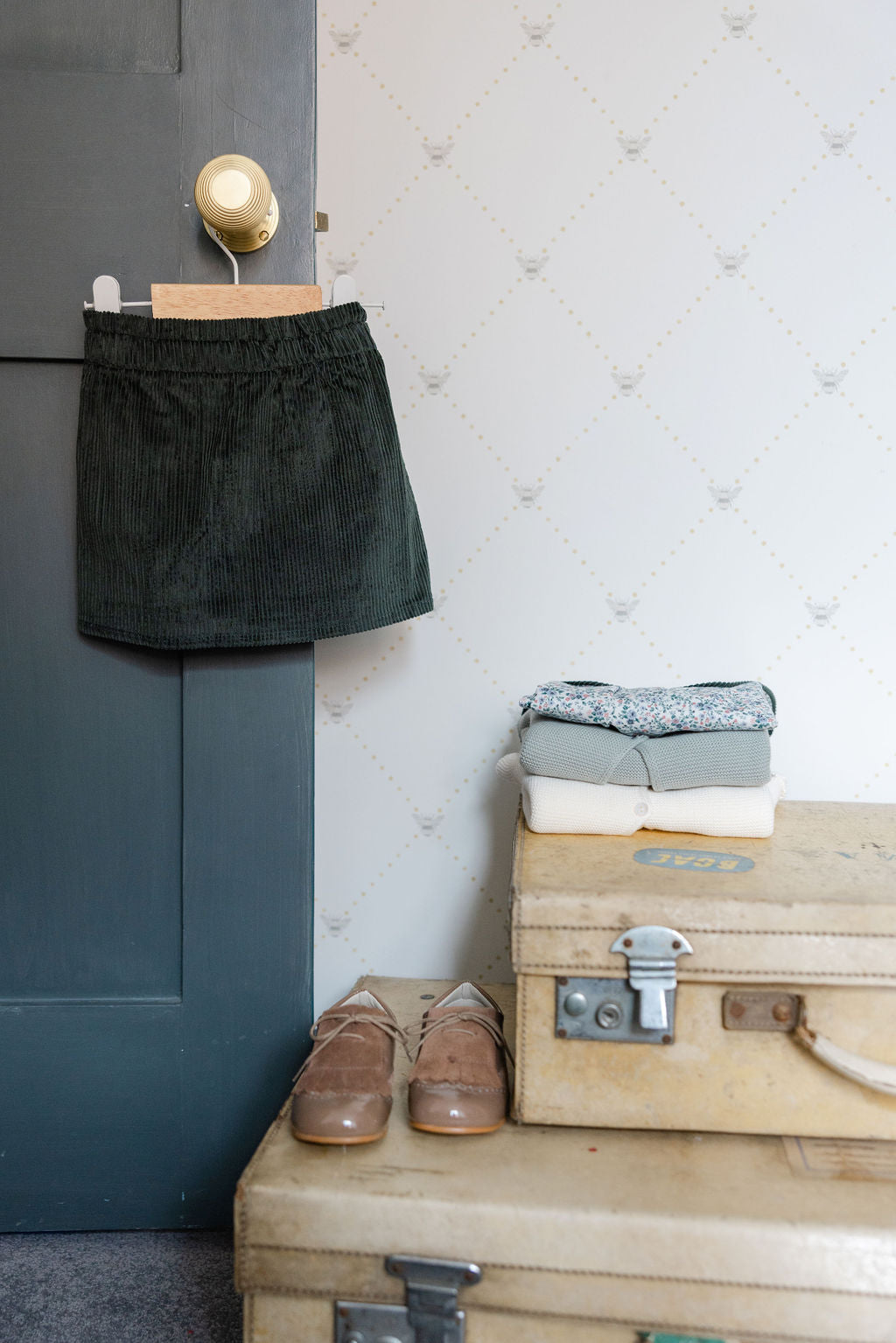 Green skirt hanging on a door next to stacked clothes and suitcases.