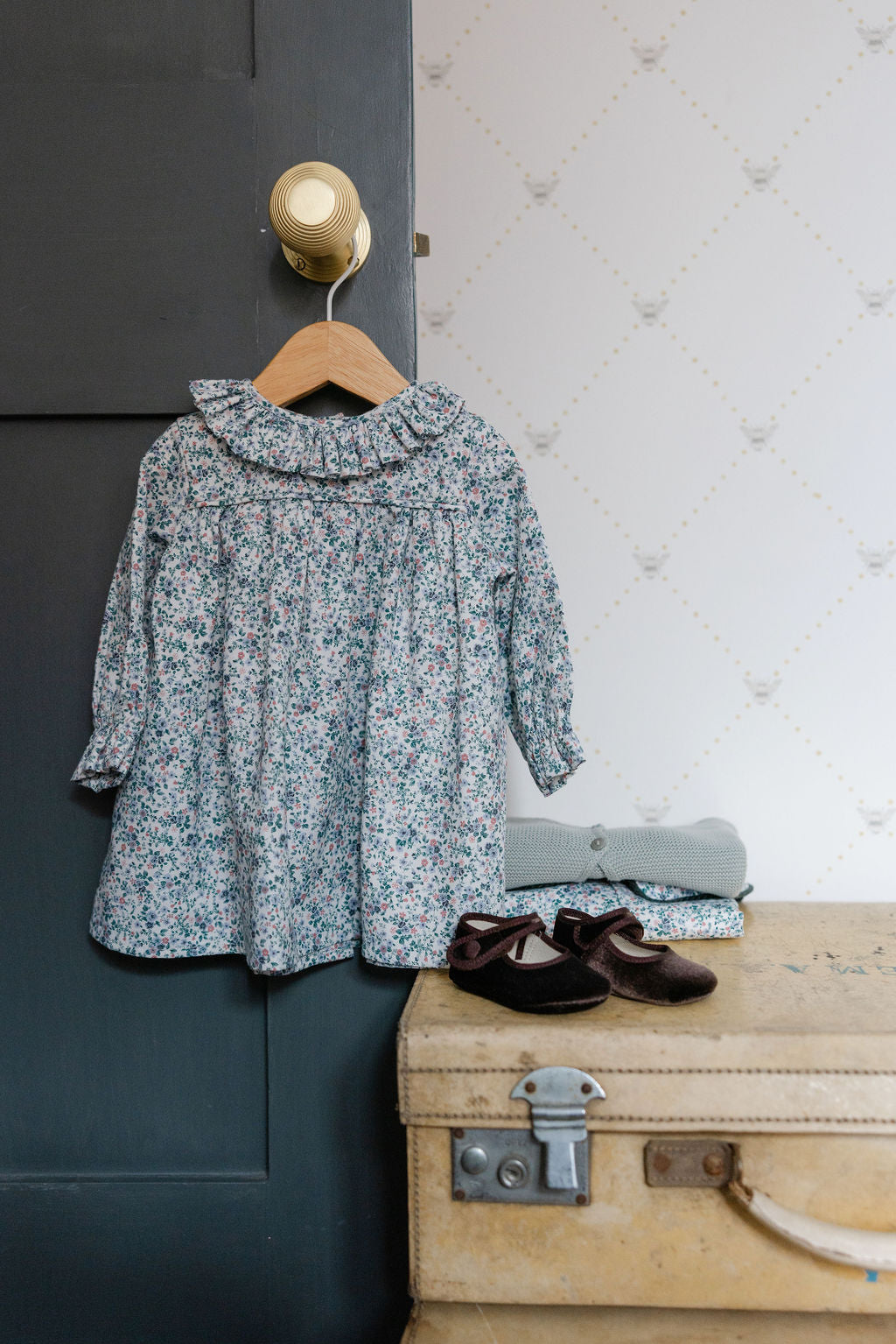 Floral dress on a hanger next to a suitcase with shoes on a textured wall background