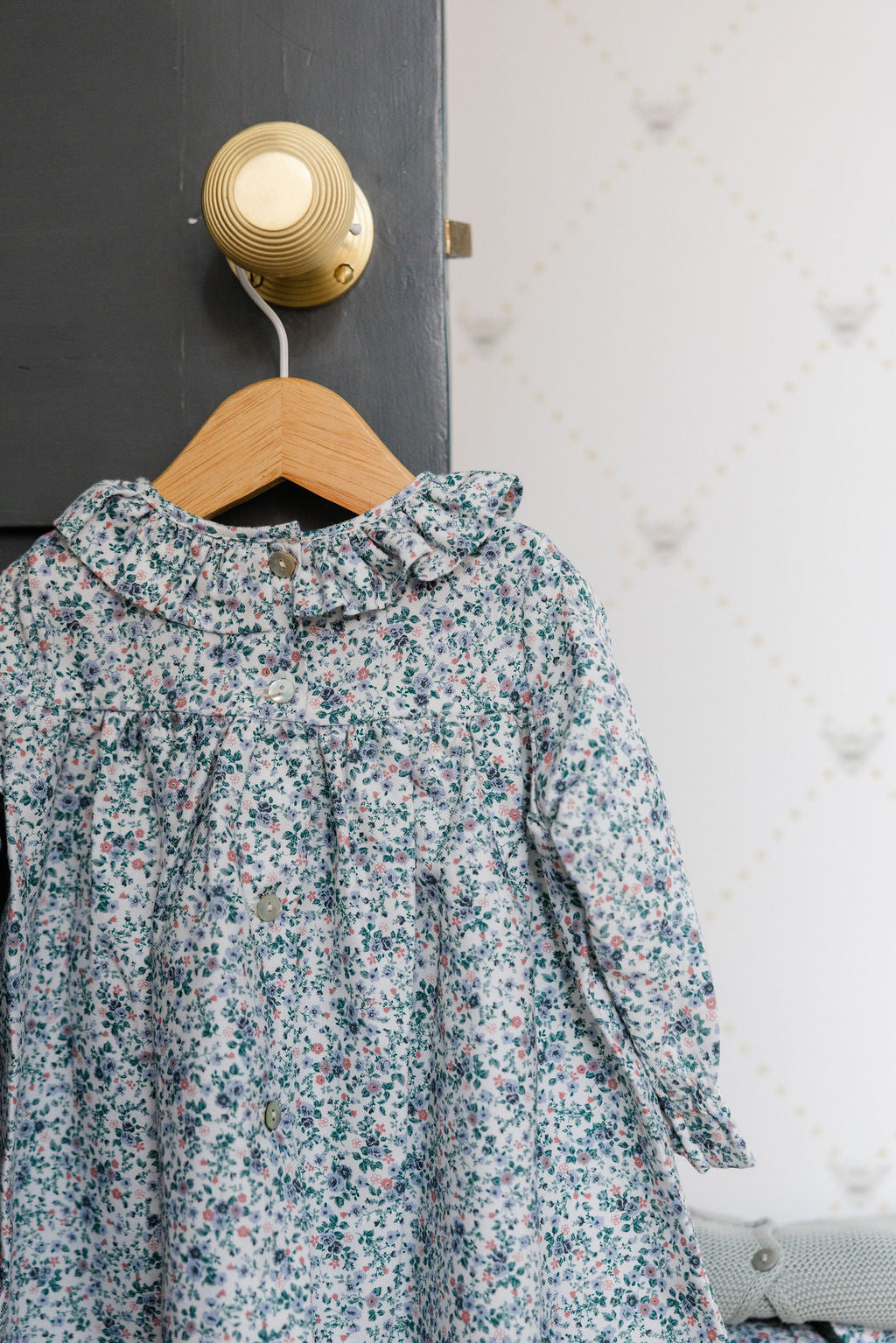 Floral dress hanging on a wooden hanger against a textured wall.
