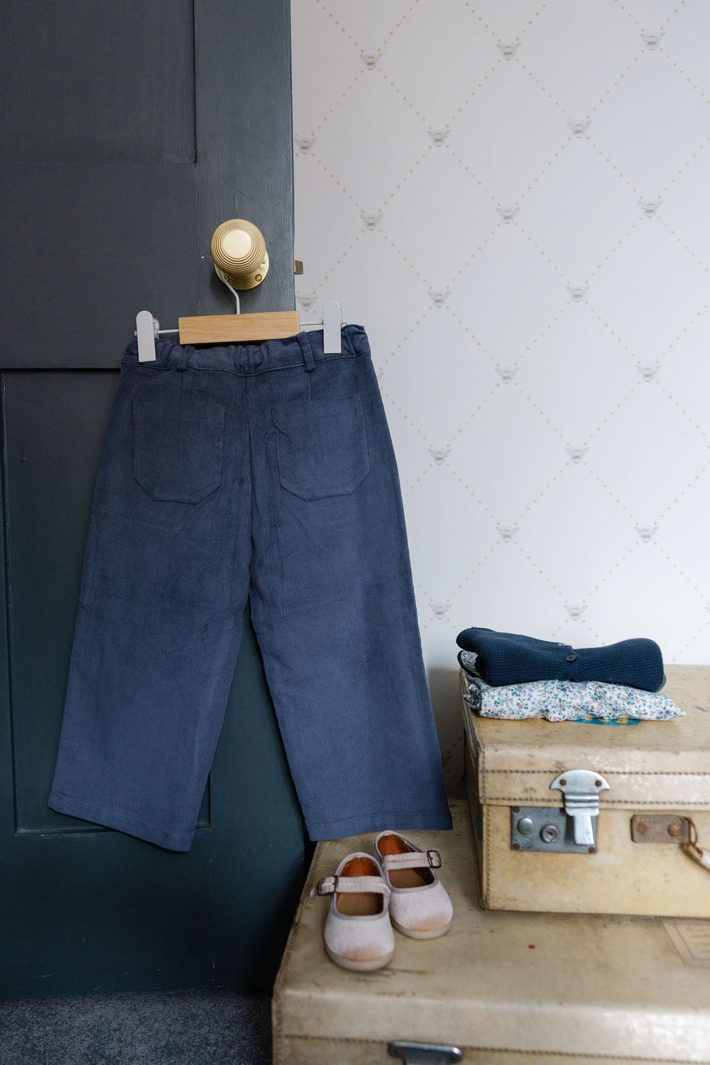 Navy blue pants hanging on a hook with a wooden chest and shoes in the background.