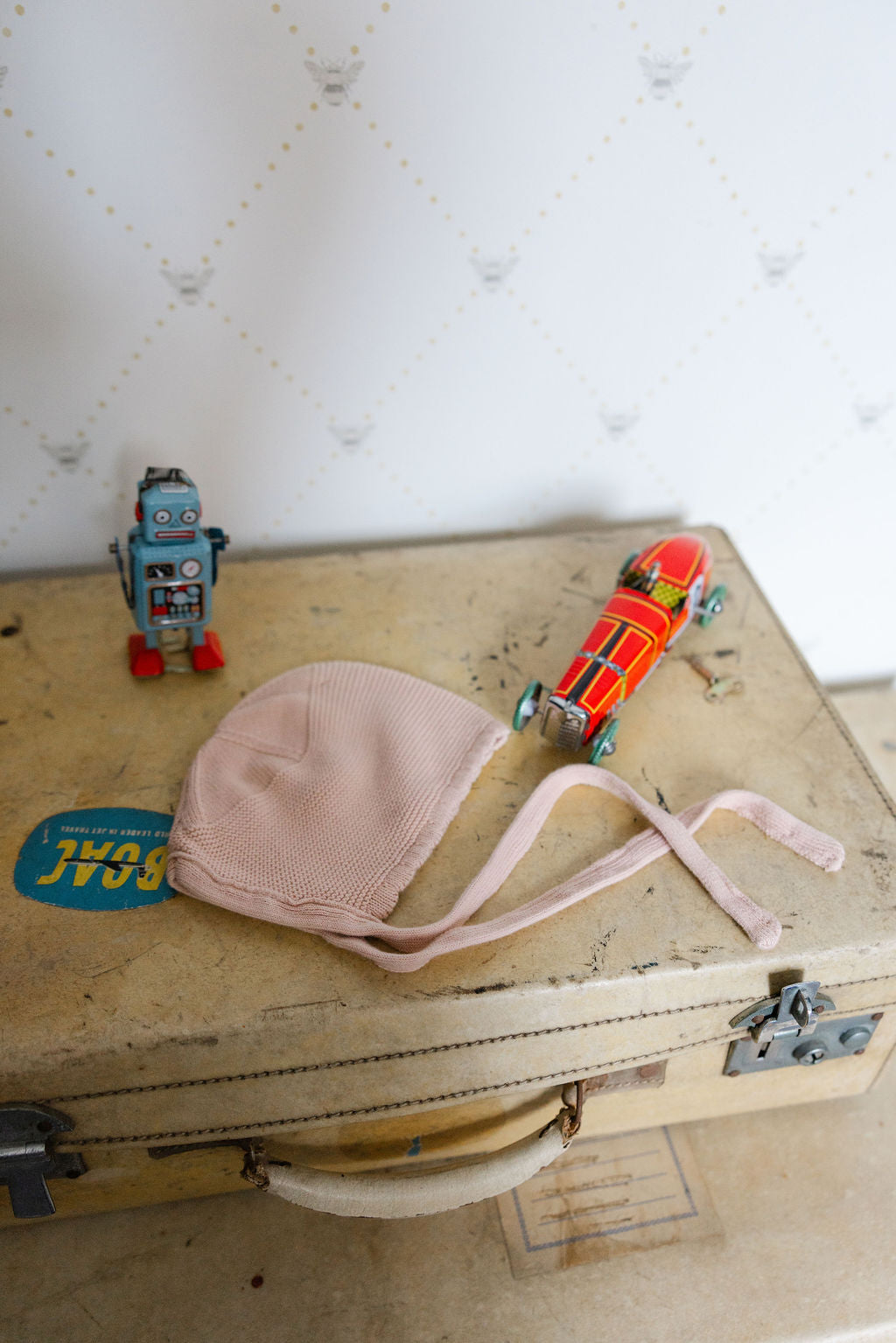 Vintage suitcase with a pink baby bonnet, toy car, and robot on a textured white background