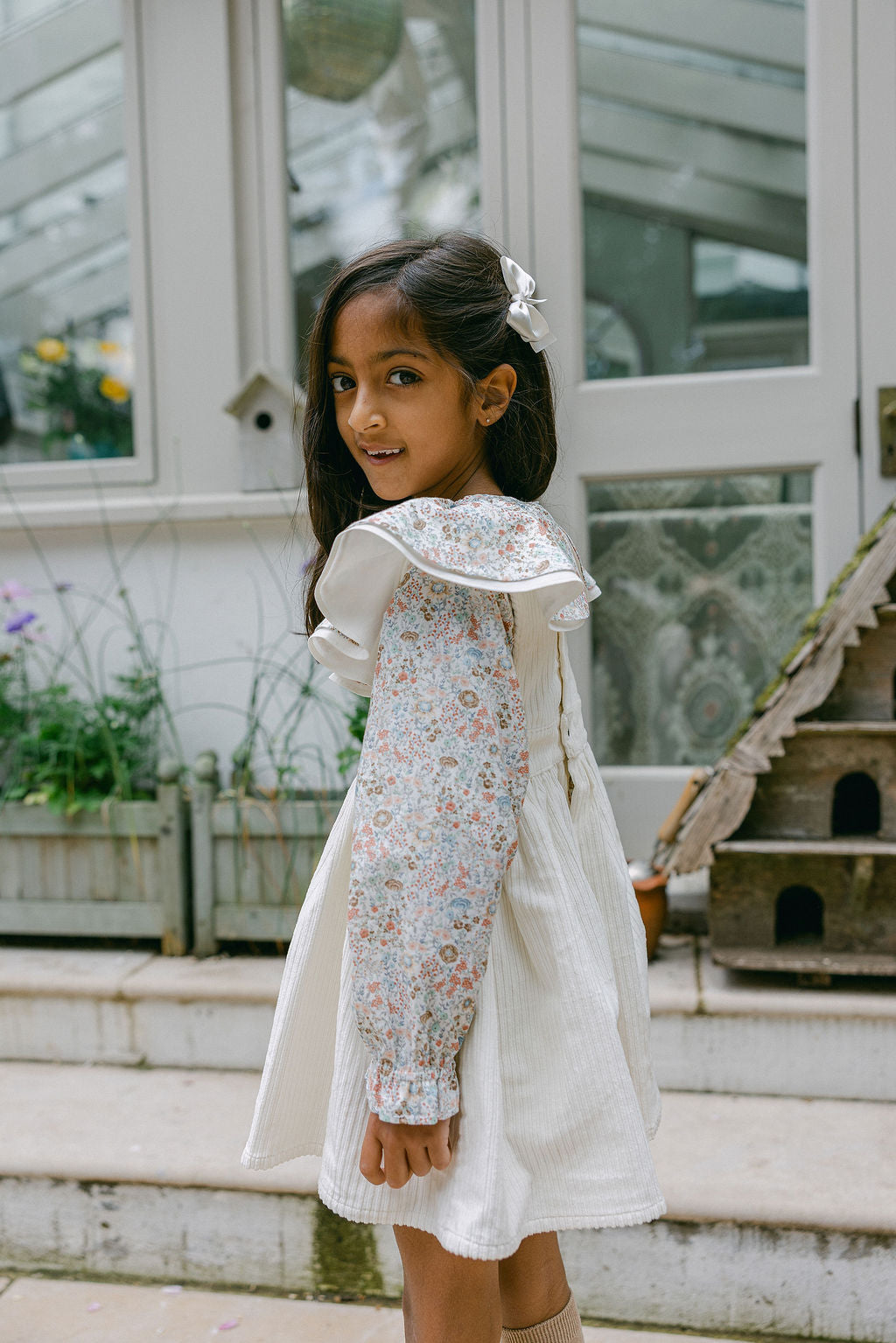 Young girl in a floral dress with a white cape standing outdoors.