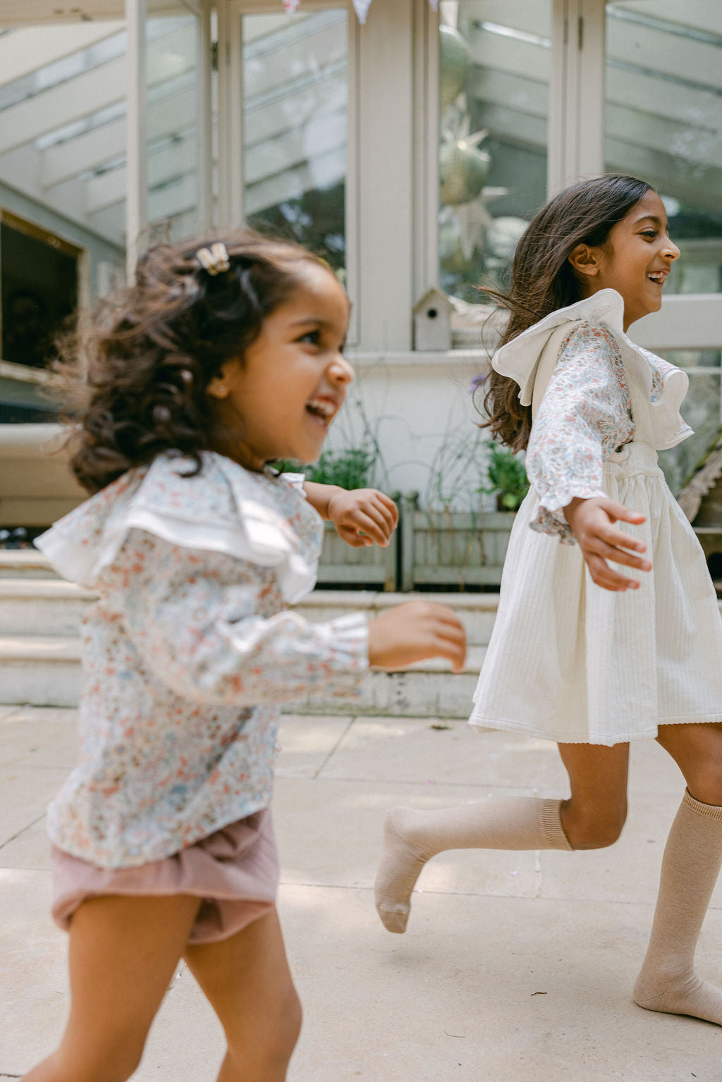 Two young girls in floral outfits running outdoors.
