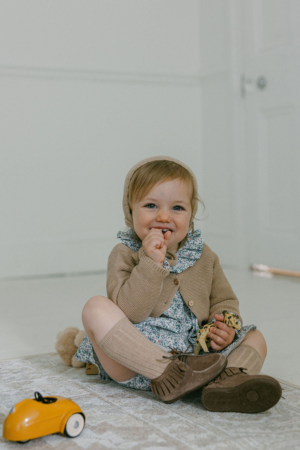 Child sitting on the floor with a toy car, wearing a brown outfit.