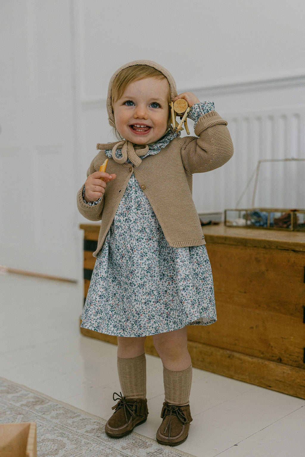 Child wearing a floral dress with a brown cardigan and boots indoors.