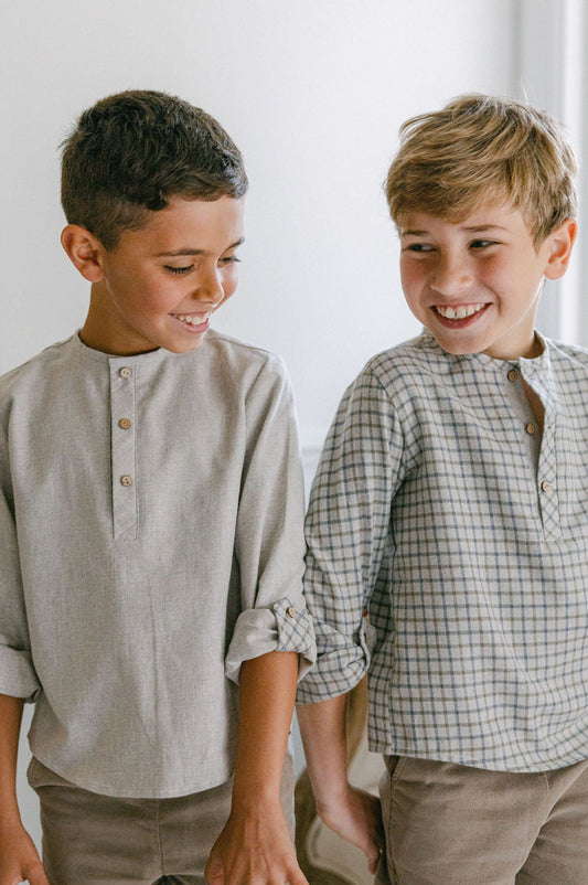 Two young boys standing side by side, smiling and wearing matching outfits.