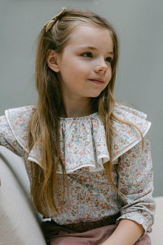 Young girl wearing a floral blouse with ruffled collar against a neutral background