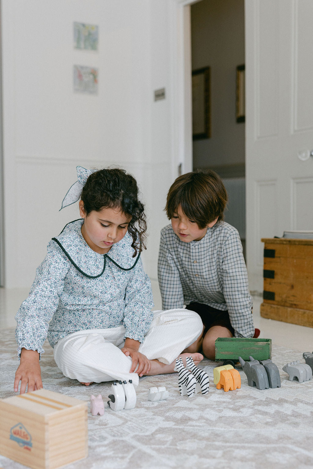 Two children playing with toys on a carpeted floor in a home setting.