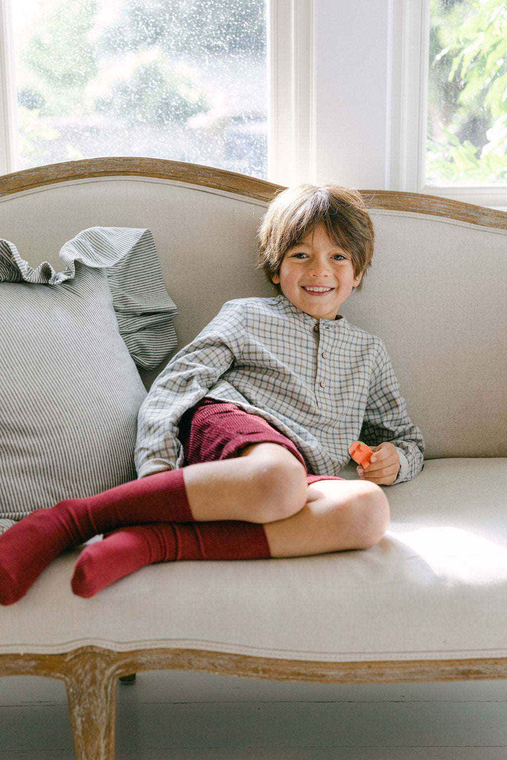 Child sitting on a beige sofa with a window in the background