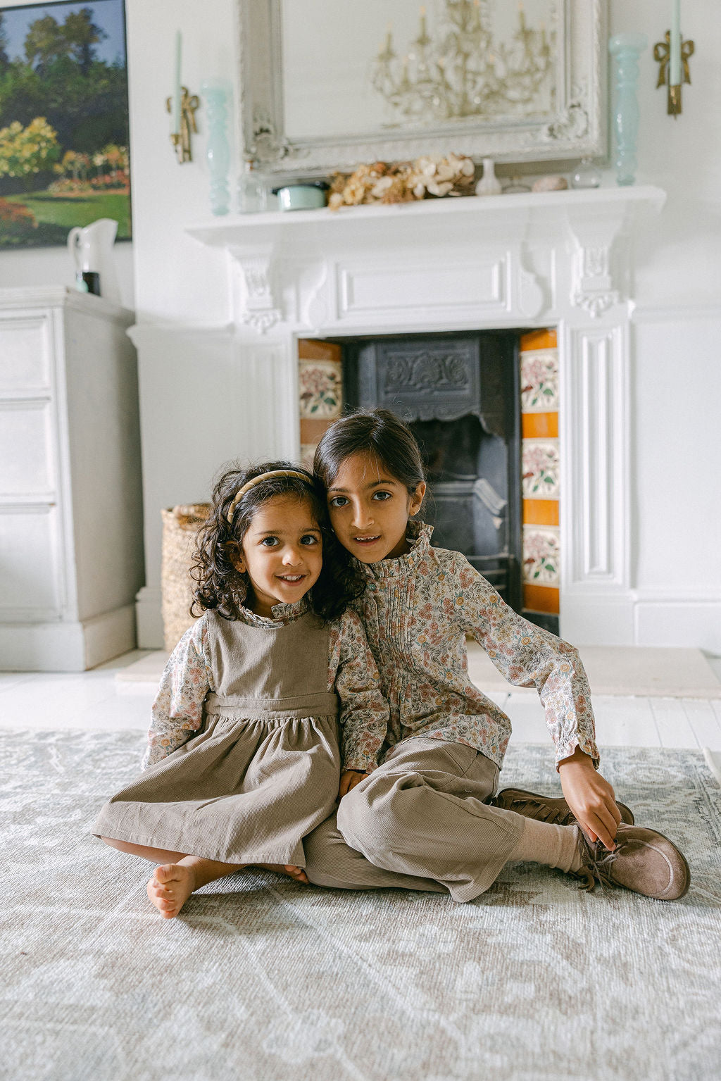 Two children sitting on the floor in a room with a fireplace and decorative items.