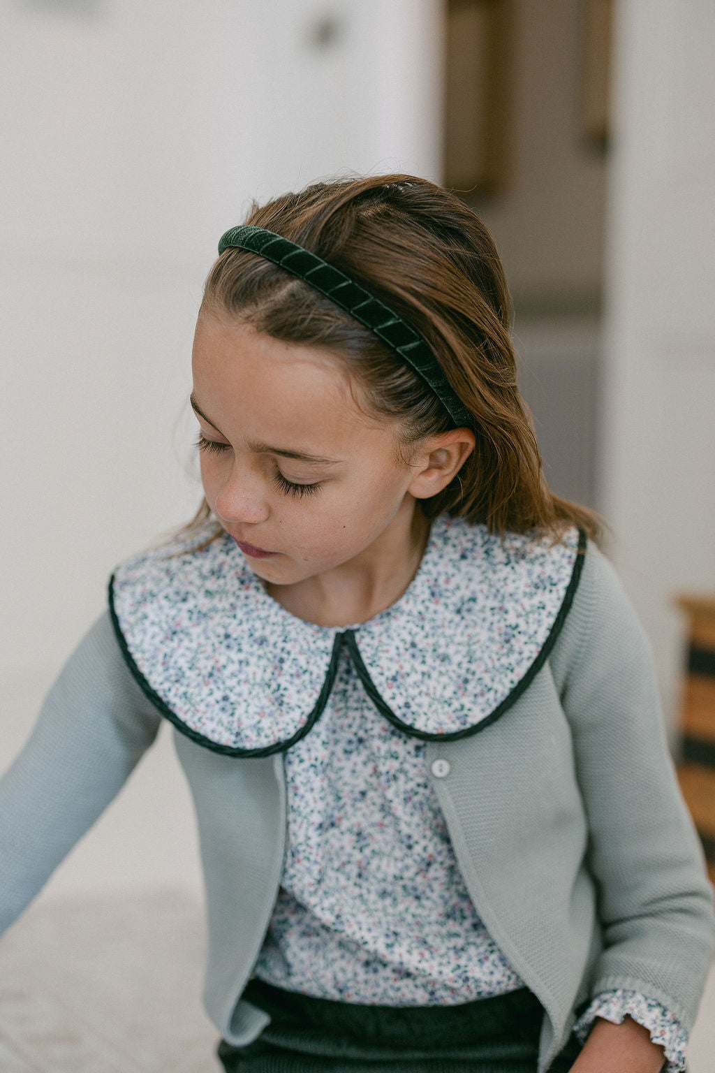 Young girl wearing a light blue cardigan with a floral collar and patterned blouse.