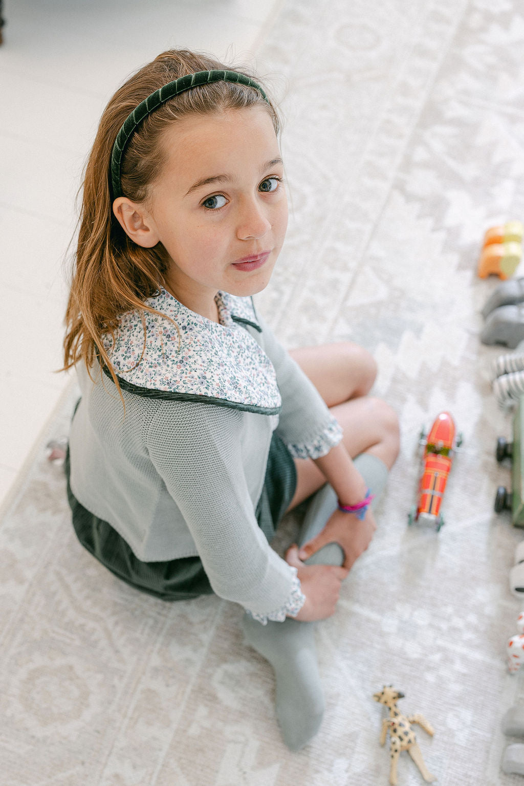Young girl sitting on a textured floor with toys around her