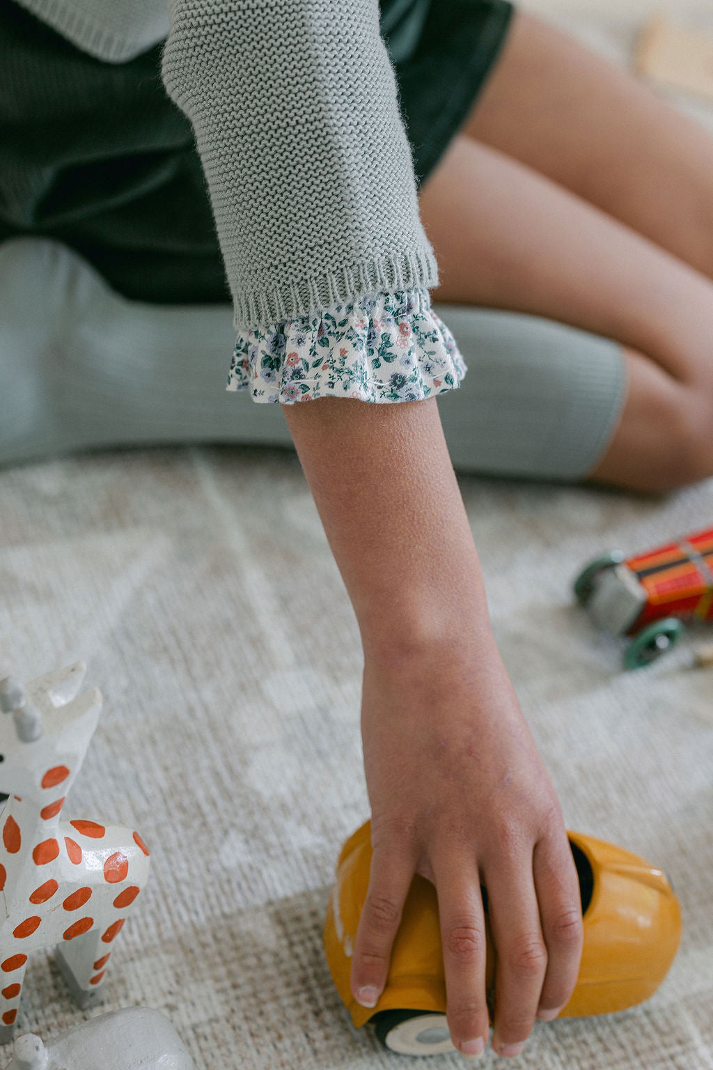 Child's hand holding a toy car on a carpeted floor with toys around