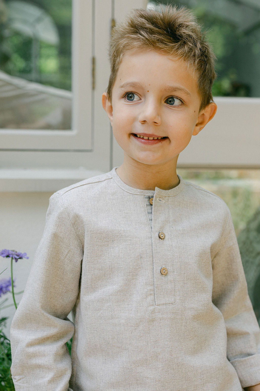 Young boy wearing a beige long-sleeve shirt with buttons, standing indoors.