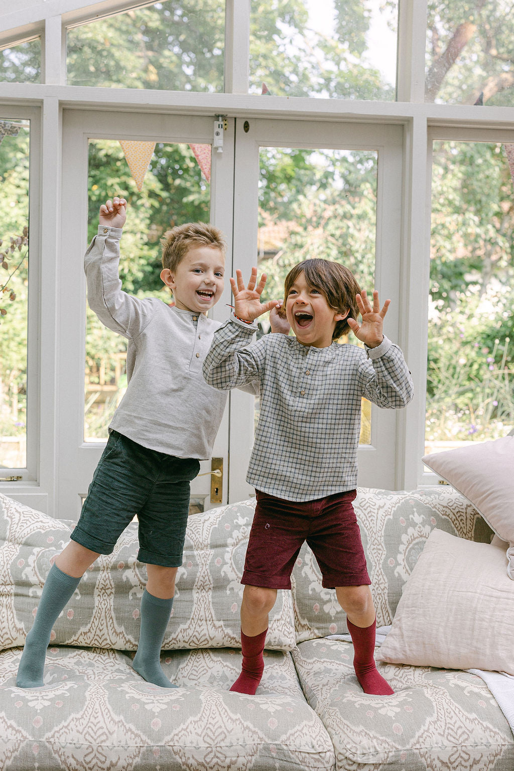 Two children playing on a couch with a large window in the background