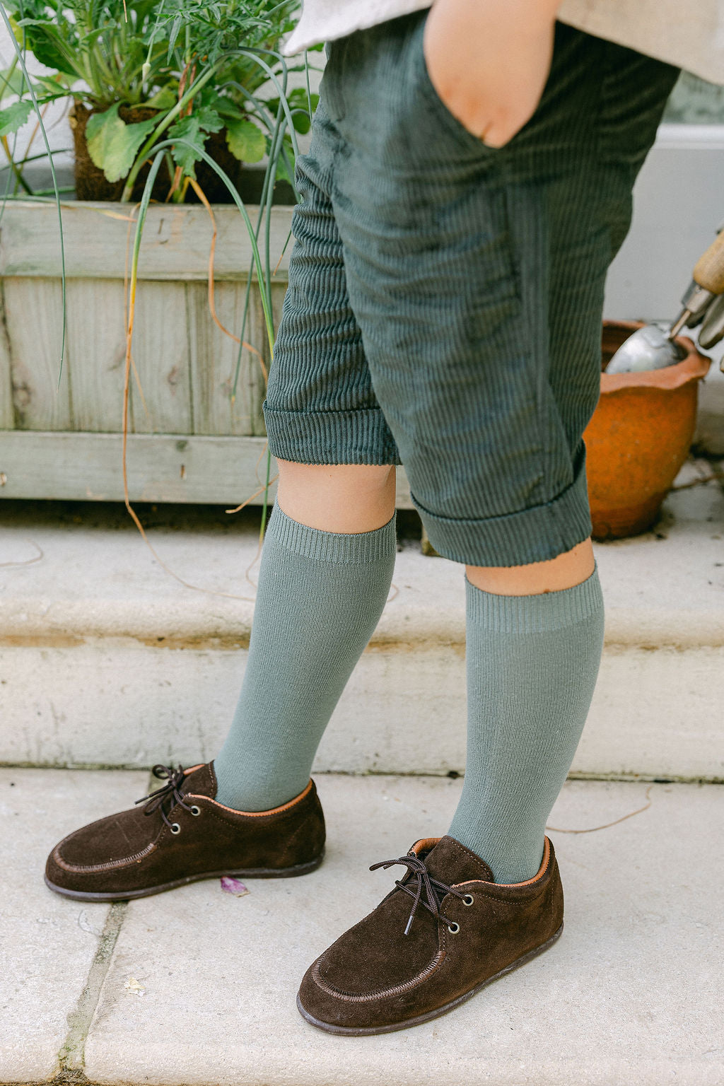 Person wearing green shorts, gray knee-high socks, and brown shoes on a stone surface.