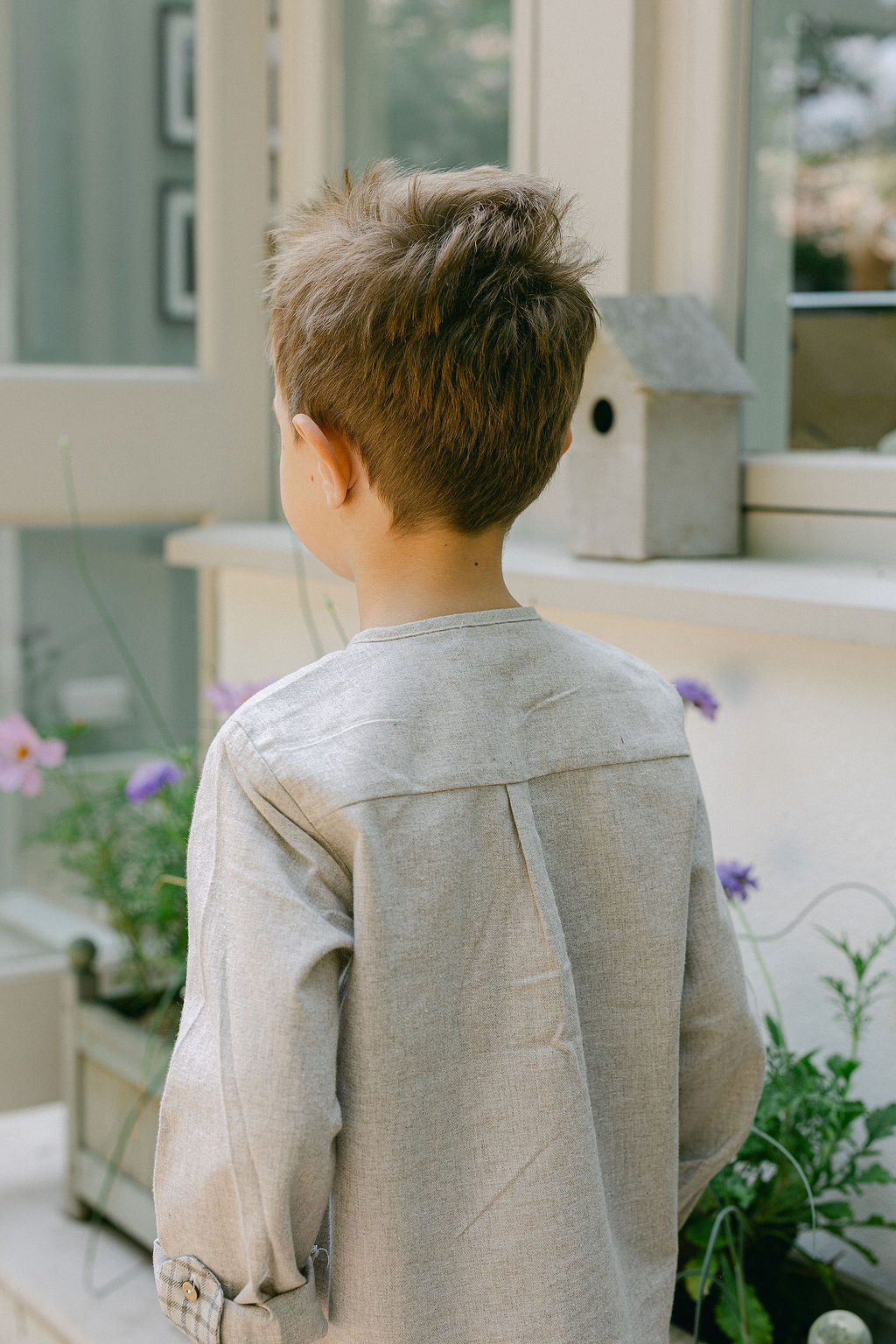 Child standing on a balcony with plants and a birdhouse in the background