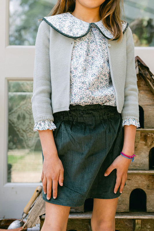 Person wearing a sequin top, gray cardigan, and green skirt outdoors.